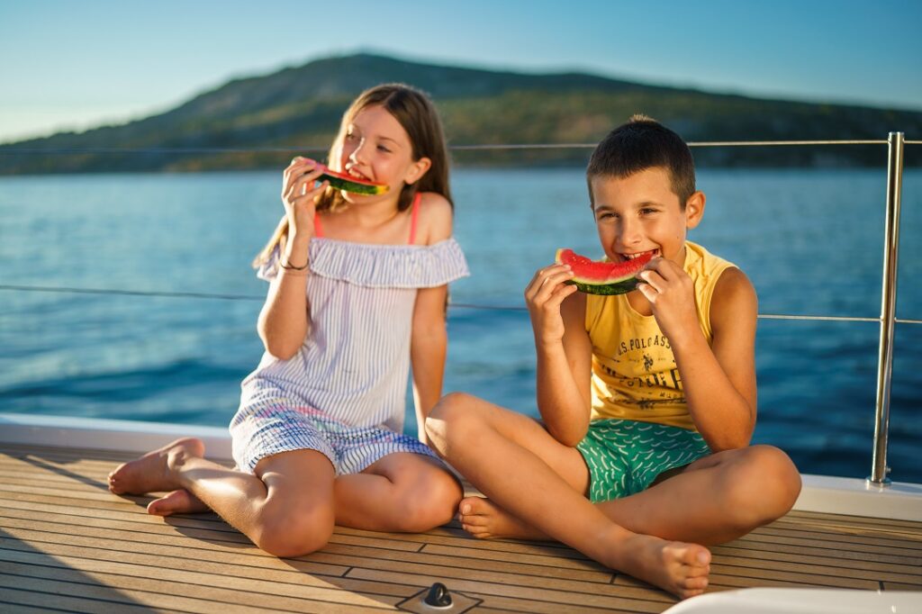 Zwei Kinder essen Wassermelone auf einem Segelbootdeck